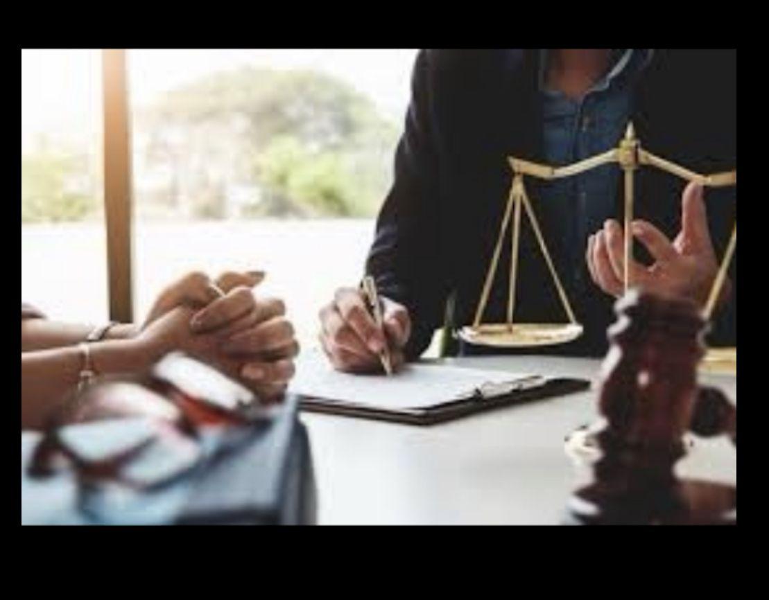 Two people discussing legal documents with scales of justice and gavel on a table.