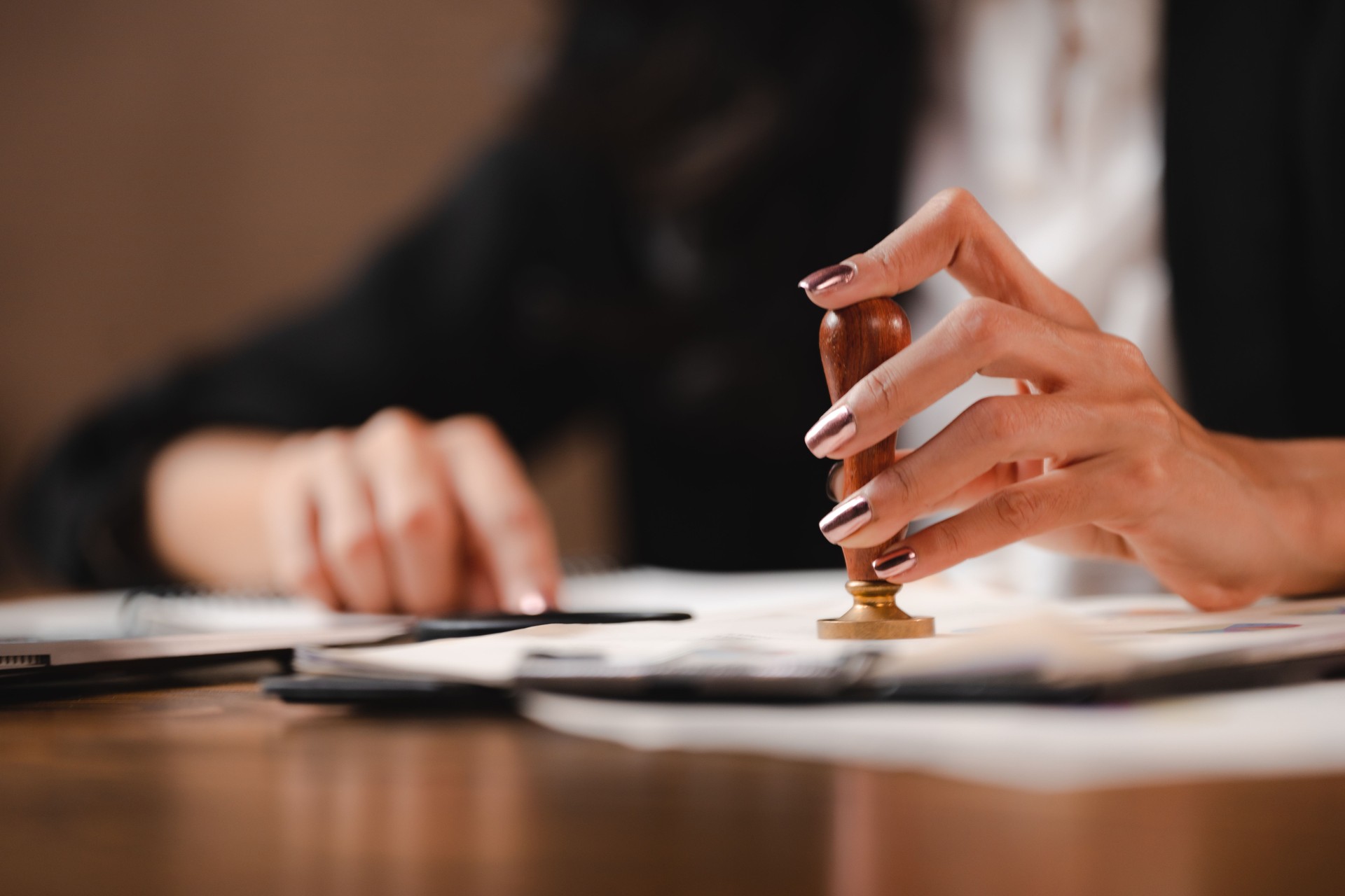 Person's hand stamping with approved stamp on certificate document public paper agreements at desk of notary or business people work, businesswoman making a signs permit on paper work business success